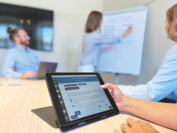 Tablet mit AC-Smart während einer Trainee-Diagnostik, im Meeting werden Ergebnisse am Whiteboard diskutiert