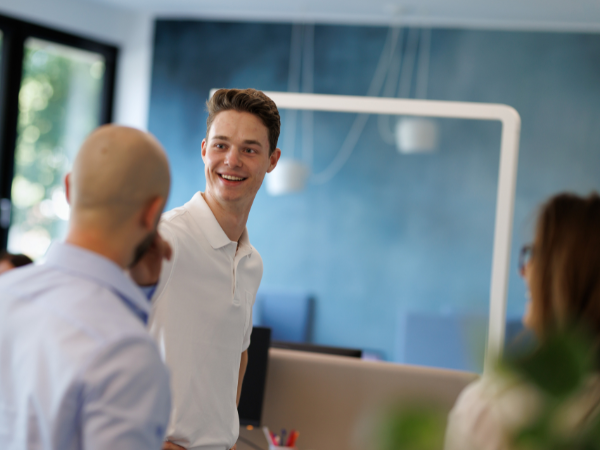 Eine Person lächelt während eines Gesprächs mit Kolleginnen und Kollegen in einem modernen Büro
