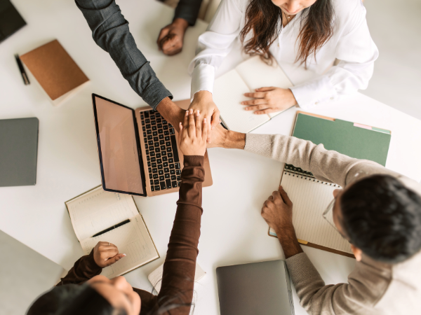 Team legt im Meeting gemeinsam die Hände zusammen als Symbol für Vertrauen, Zusammenhalt und psychologische Sicherheit